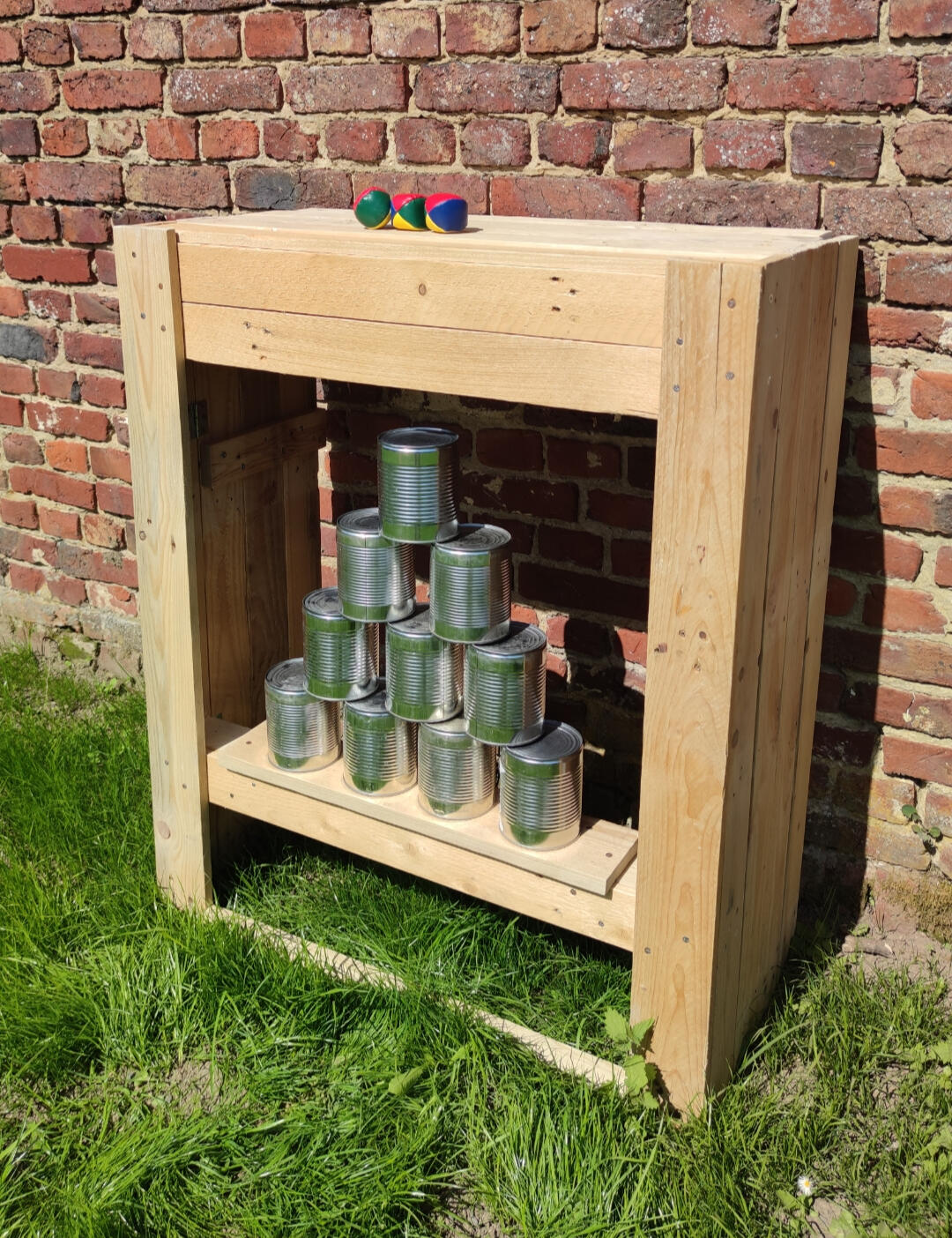 Chamboule tout Piko Event | Photo du jeu chamboule tout, posé dans l'herbe sans support pour être à hauteur d'enfant en bas âge. Jeu en bois loué pour anniversaire