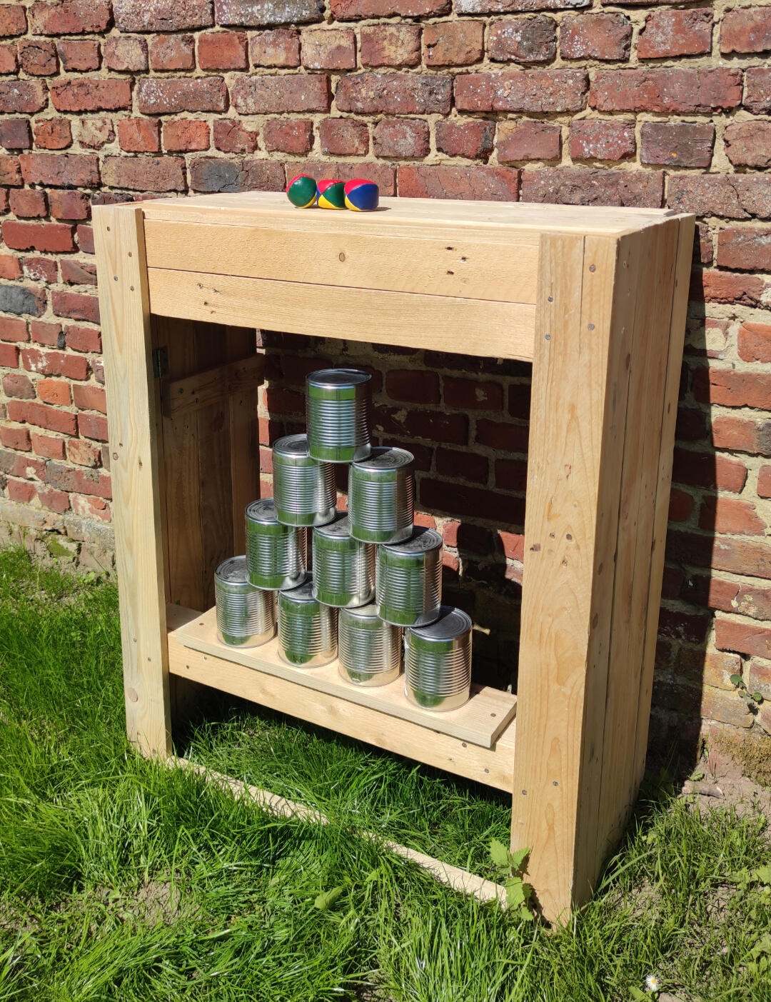 Piko Event | Photo du jeu chamboule tout, posé dans l'herbe sans support pour être à hauteur d'enfant en bas âge. Jeu en bois loué pour anniversaire. Lien vers les règles du jeu