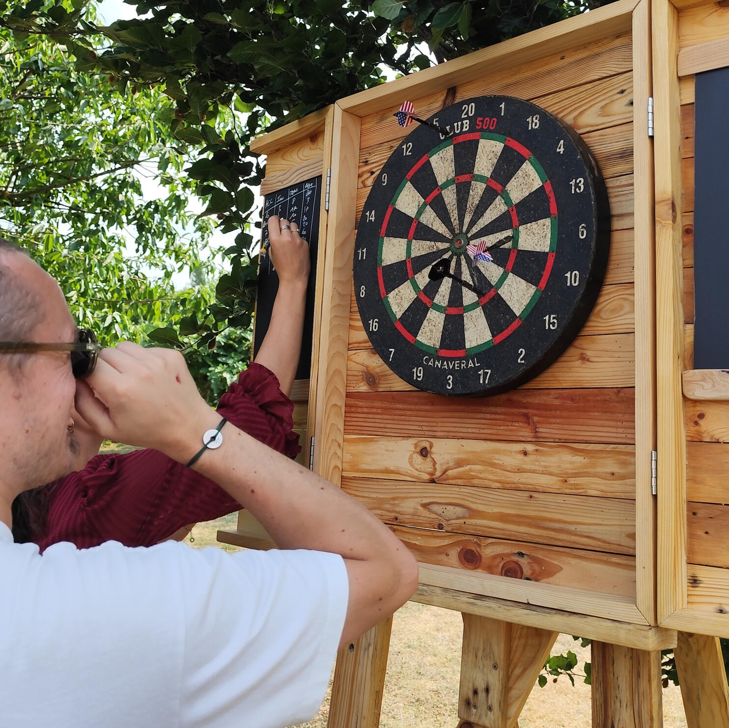Cible de fléchettes Piko Event | Photo du jeu cible de fléchettes, zoomée sur trois fléchettes avec drapeau américain plantées dans la cible. Jeu sur support en bois